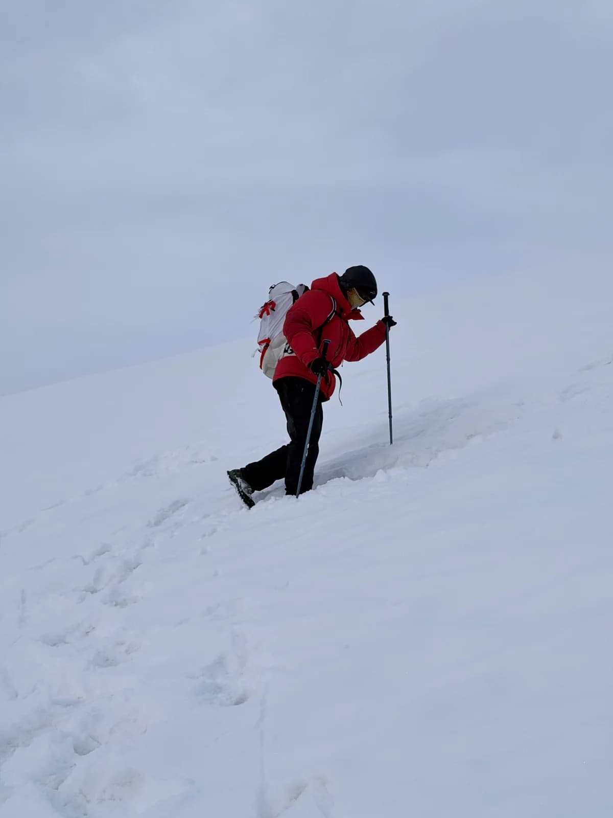 Climber using a pole on a snow-covered slope in low visibility