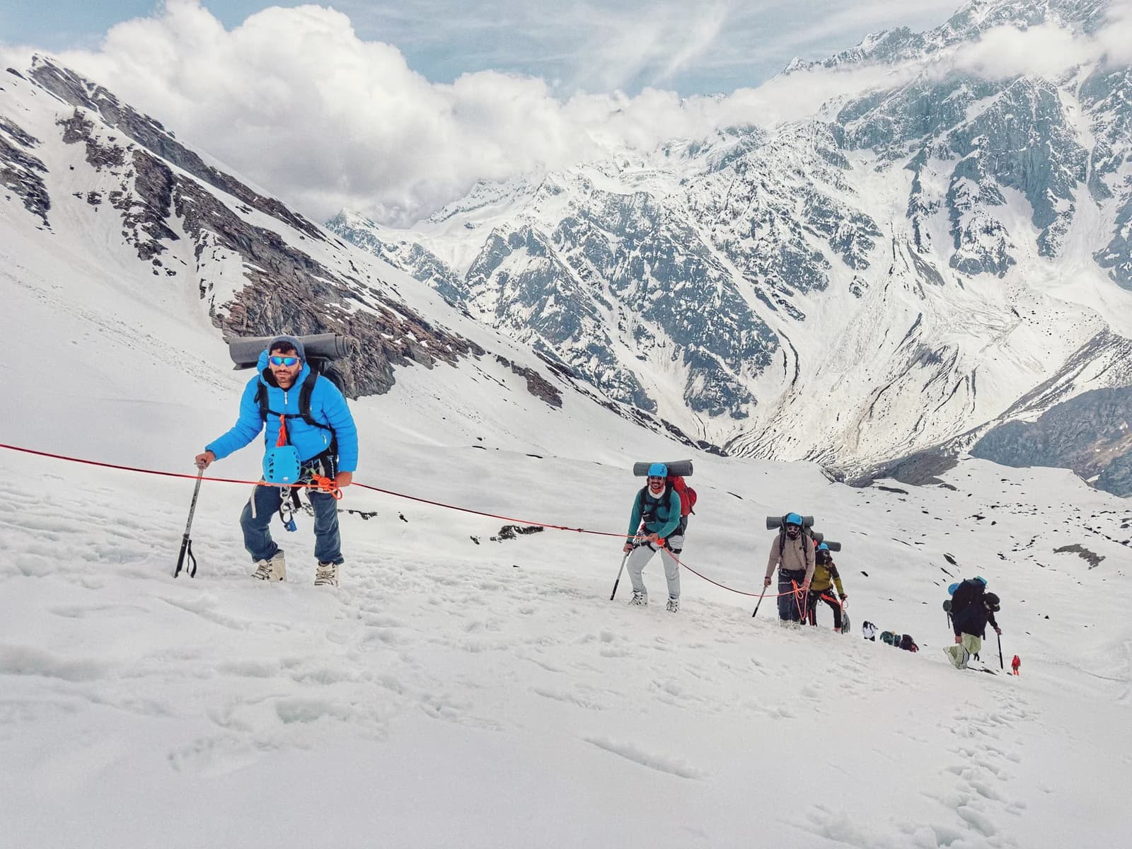 Climbers carrying packs and ice axes while moving along a rope on snow
