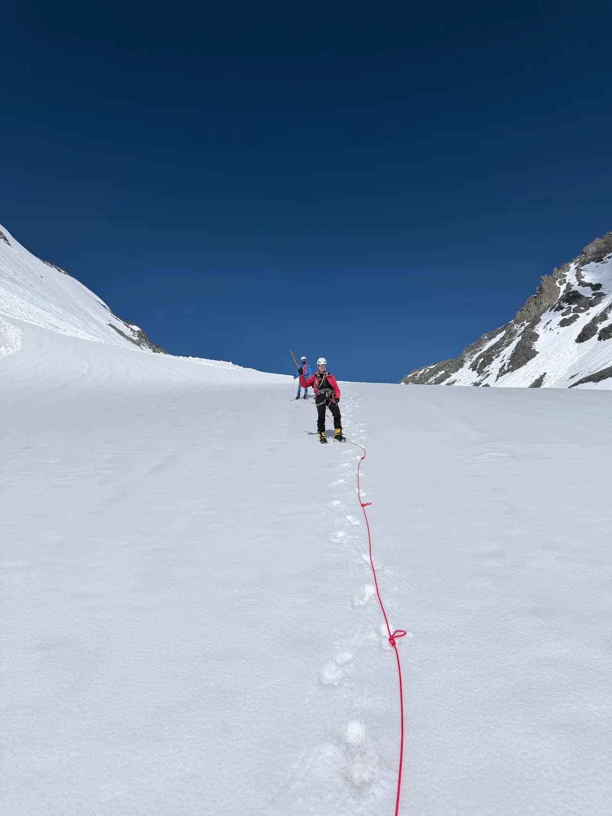 Two roped climbers on a snow slope beneath a clear blue sky